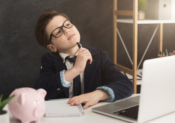 Boy sitting in front of his laptop computer looking upward in thought.