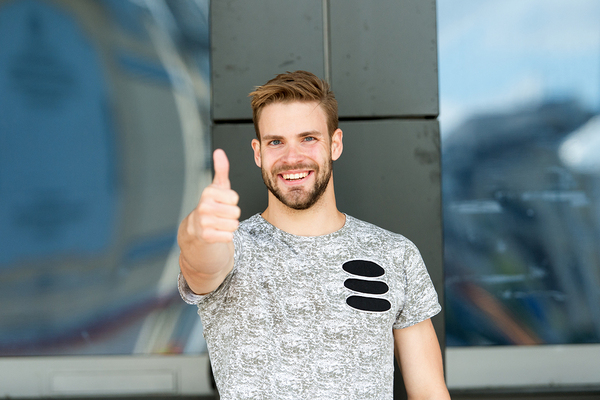 Happy man standing against a stone wall with thumbs up.